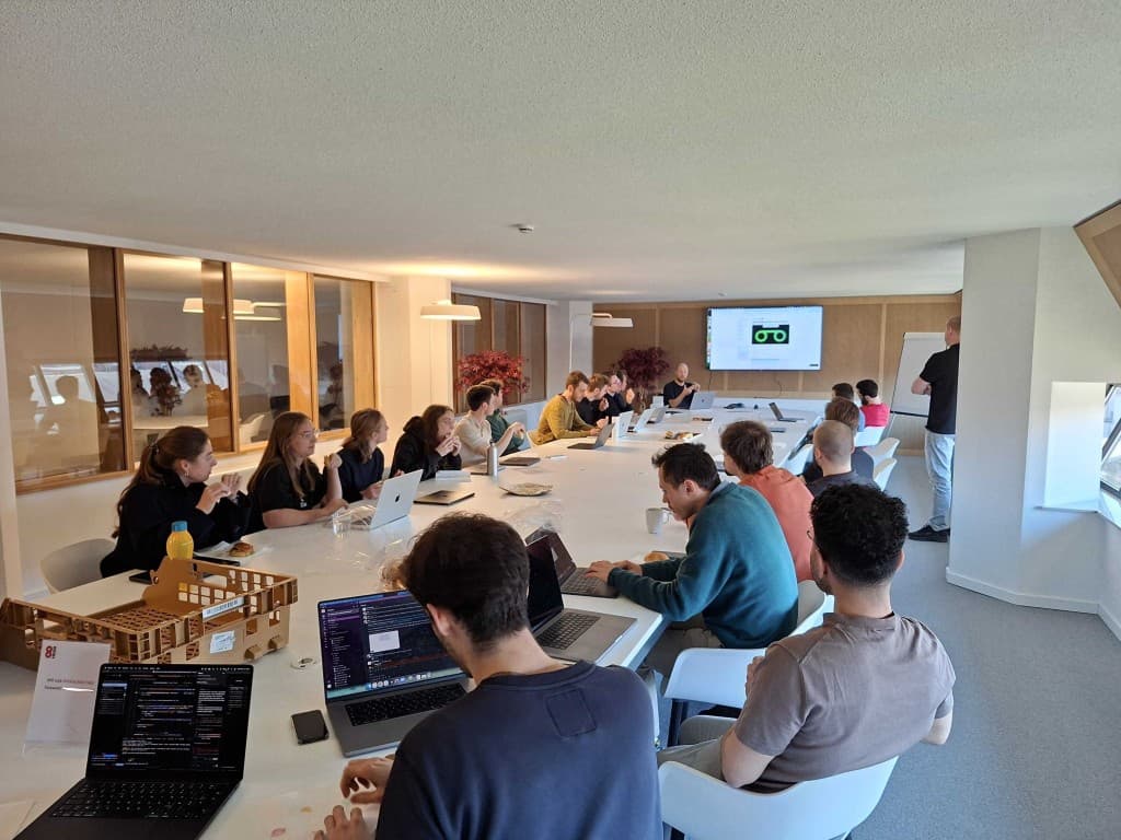 Team workshop session at a long table with laptops and presentation screen.